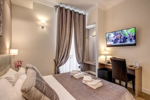 Camera moderna al Chester Suites B&B di Roma con letto, scrivania, TV e tende beige