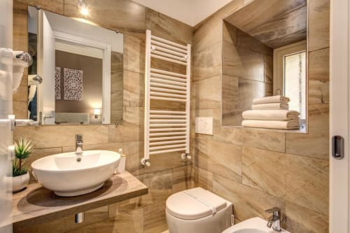 Bagno moderno a Chester Suites Roma con piastrelle beige, lavabo a bacinella, scaldasalviette e doccia walk-in