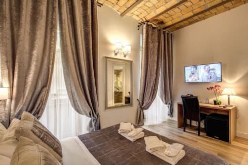 Camera elegante di Chester Suites Rome con letto matrimoniale, tende dal pavimento al soffitto, scrivania e soffitto in mattoni a vista
