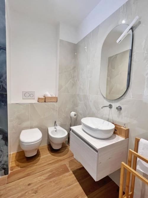 Bagno moderno presso Finella Charming Rooms a Bari con sanitari bianchi, pavimento in legno e specchio ovale