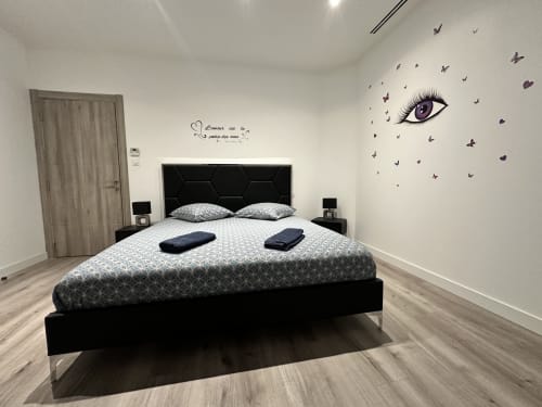 Chambre moderne aux Gîtes Les Camelias 71 avec lit à cadre noir, literie à motifs et décoration murale papillons à Oslon