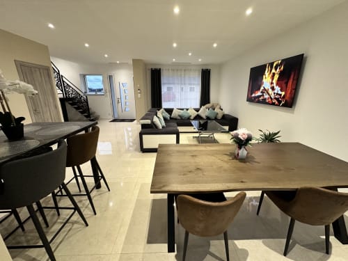 Séjour moderne ouvert aux Gites Les Camelias 71 avec table à manger, canapé noir, télévision et vue sur le jardin à Oslon