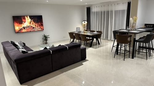 Espace de vie ouvert et moderne aux Gites Les Camelias avec canapé d'angle noir, télévision, tables de salle à manger et vue sur le jardin