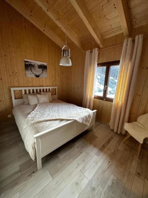 Chambre chaleureuse en bois aux Chalet d'hôtes Les Louettes, Saxon avec lit blanc, suspension et vue sur les montagnes