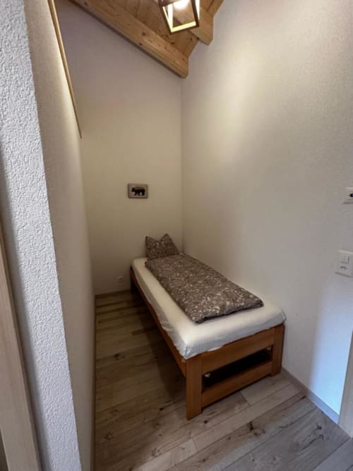 Lit simple douillet dans une petite chambre d'hôtes du chalet Les Louettes à Saxon, aux murs blancs et parquet en bois