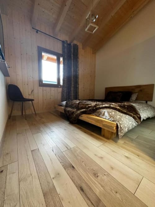 Chambre cosy en bois du Chalet d'hôtes Les Louettes à Saxon avec lit, fauteuil, fenêtre et parquet