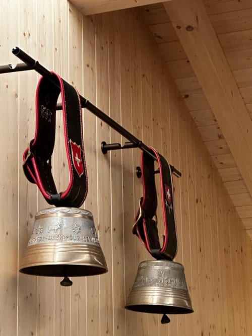 Cloches à vaches suisses traditionnelles avec rubans rouges suspendues à une poutre en bois au Chalet d'hôtes Les Louettes, Saxon