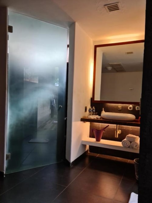 Modernes Badezimmer im Isla Tajín Beach & River Resort in Tuxpan mit Glasdusche mit Mattoptik, dunklen Bodenfliesen und Beleuchtung