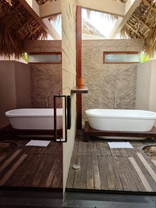 Zwei freistehende weiße Badewannen im Außenbad des Isla Tajín Beach Resort in Tuxpan mit Steinmauern und tropischem Strohdach