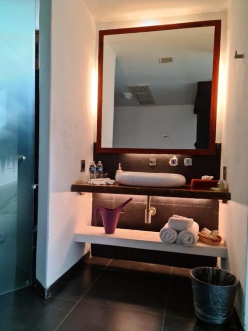 Modernes Badezimmer im Isla Tajín Beach & River Resort mit beleuchtetem Spiegel, dunklem Holzwaschtisch und weißen Handtüchern