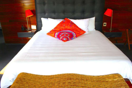 Modernes Hotelzimmer in Isla Tajín mit weißem Bett, farbigen Dekokissen, roten Lampen und dunklem Kopfteil in Tuxpan