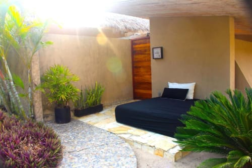 Outdoor bedroom at Isla Tajín Beach & River Resort in Tuxpan with black bed, tropical plants, and wooden door under thatched