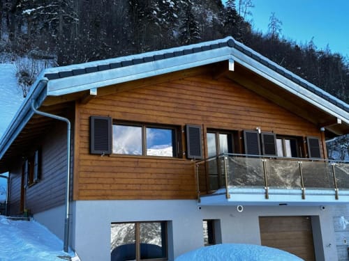 Chalet alpin moderne avec étage supérieur en bois et base en pierre blanche dans un cadre montagneux enneigé de Saxe, Suisse
