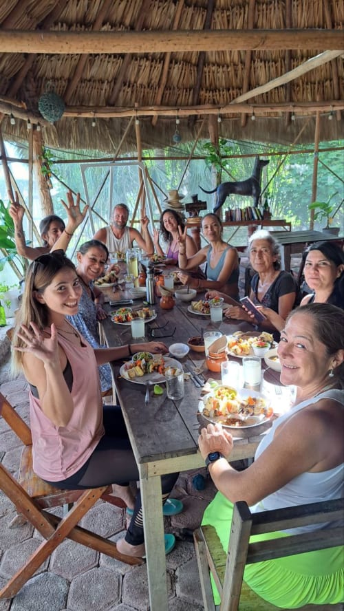 Comensales disfrutando de una comida grupal en el hostel Cayuco Maya en Bacalar, México, bajo un techo de palapa tejida