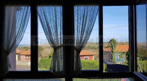 View from Esto si es vida hotel in Ribadesella through blue curtains overlooking rural landscape with red-roofed houses