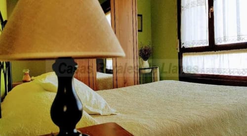 Dormitorio luminoso en el hotel Esto si es vida en Ribadesella con lámpara amarilla, paredes verdes y luz natural de las ventanas
