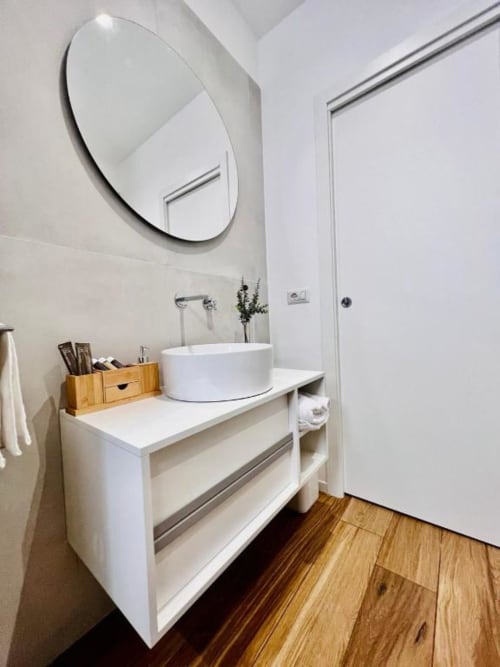 Bagno moderno a Finella Charming Rooms a Bari con specchio rotondo, lavabo bianco, pavimento in legno e arredamento minimalista
