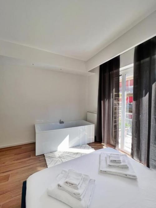Camera elegante di Finella Charming Rooms a Bari con vasca bianca, parquet, tende nere e vista balconata sulla città