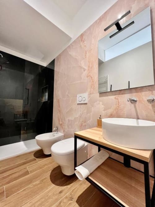 Bagno moderno a Finella Charming Rooms Bari con pareti in marmo, lavabo ovale bianco, wc e mobiletto in legno