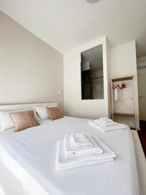 Camera da letto moderna e luminosa a Finella Charming Rooms a Bari con biancheria bianca, cuscini marroni e specchio con vista sulla città