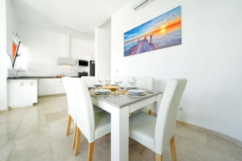 Comedor moderno con sillas y mesa blancas en Villa Cacemar Maspalomas, cocina visible al fondo