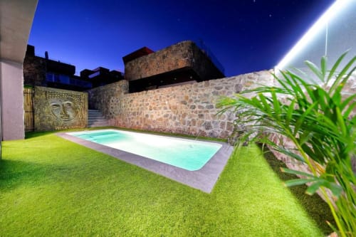 El patio con piscina privada de Villa Cacemar en Maspalomas de noche, con muros de piedra iluminados, piscina color turquesa y exuberante vegetación