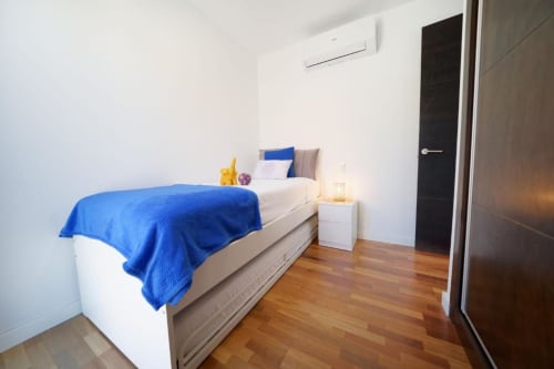 Dormitorio moderno con ropa de cama azul, suelos de madera, paredes blancas, aire acondicionado y lámpara de mesita en Villa Cacemar, Maspalomas