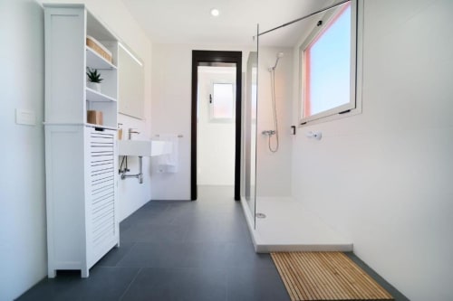 Baño moderno en la villa Cacemar con ducha tipo walk-in, mueblería blanca, piso de azulejo oscuro y tapete de madera en Maspalomas