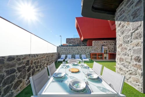 Terraza comedor de Villa Cacemar con mesa puesta, muros de piedra, detalles arquitectónicos rojo y vistas al jardín en Maspalomas