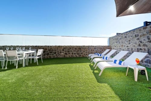 Terraza en la azotea de Villa Cacemar en Maspalomas con tumbonas, zona de comedor, césped artificial y muros de piedra bajo cielo azul