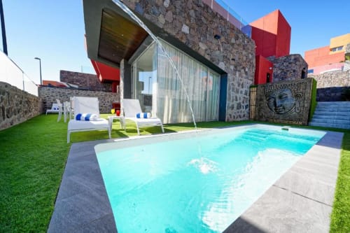 Villa moderna en Maspalomas con piscina privada color turquesa, tumbonas, muros de piedra y elementos arquitectónicos rojos en el jardín