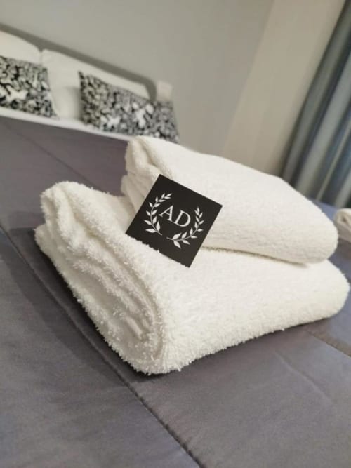 Asciugamani bianchi arrotolati con etichetta AS Trastevere su letto grigio nella guest house di Roma