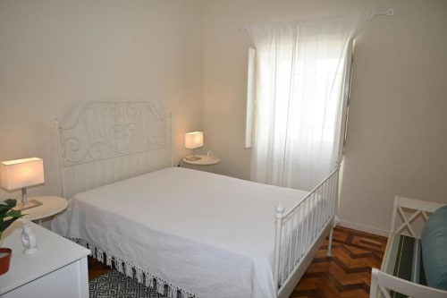 Chambre lumineuse à la Villa Sor à Ponte de Sor avec lit métallique blanc, draps blancs, tables de nuit et rideaux voilage