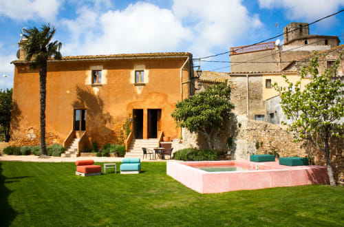 Bâtiment rustique orange vif avec pelouse verte, mobilier coloré et piscine aux Apartmentos Rectoria de Regencós, Girona