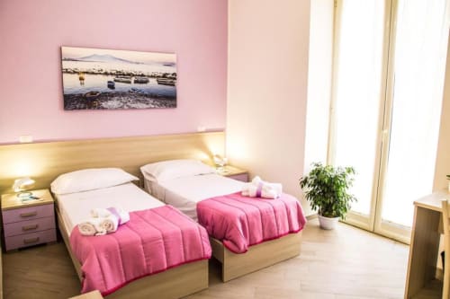 Camera doppia del Borgo Angioino B&B Napoli con pareti rosa, letti in legno e opere d'arte con vista mare