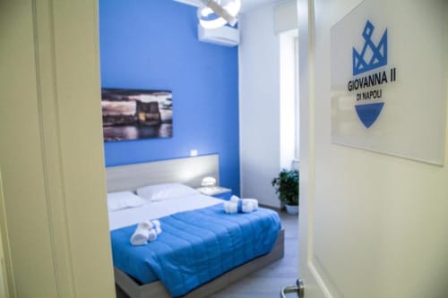 Camera da letto blu con vista sulla città presso il Borgo Angioino BnB a Napoli, con biancheria blu e targhetta Giovanna II