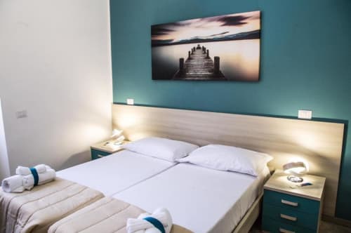 Dormitorio moderno en tonos azul verdoso y madera clara en Borgo Angioino Nápoles con cama doble, obra de arte de muelle urbano e iluminación ambiental