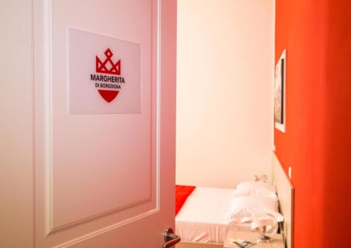 Entrada de la habitación Margherita di Borgogna en Borgo Angioino B&B Nápoles, con paredes rosas y puerta roja con logo de corona