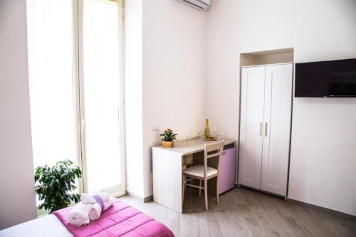 Dormitorio rosa brillante en un B&B de Nápoles con TV, escritorio, armario y vista a la ciudad desde las puertas del balcón