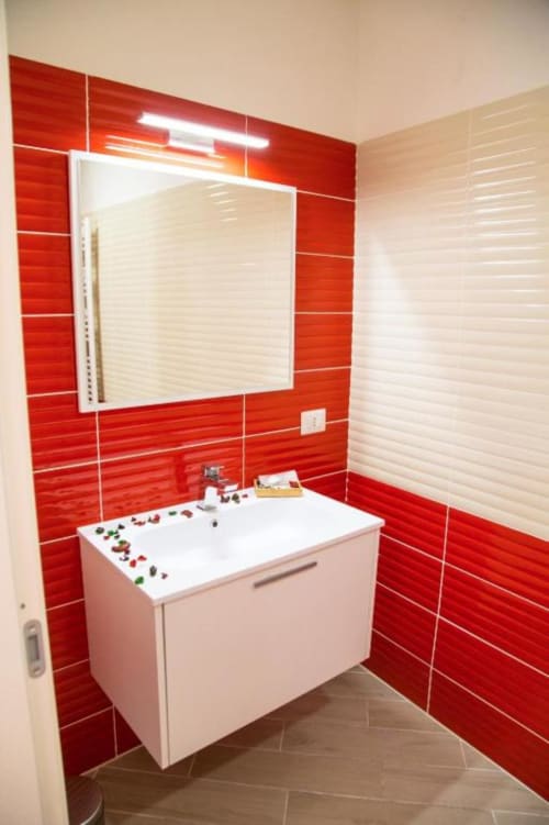 Baño moderno con paredes de azulejos rojos, lavamanos blanco y espejo iluminado en B&B Borgo Angioino Nápoles