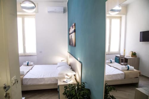 Dos dormitorios modernos en Borgo Angioino B&B en Nápoles, separados por pared azul petróleo, con camas gemelas y vistas a la ciudad