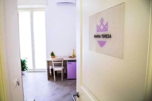 Entrada a la habitación Maria Teresa en Borgo Angioino B&B en Nápoles, mostrando cocineta y logo corona púrpura