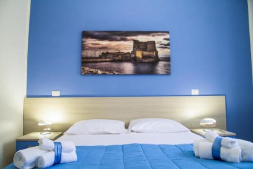 Dormitorio moderno con pared azul de acento, almohadas blancas y fotografía de la ciudad en Borgo Angioino B&B en Nápoles