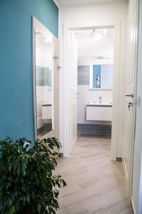 Pasillo de baño moderno en el hotel Borgo Angioino de Nápoles con paredes turquesas, accesorios blancos y suelos de imitación madera