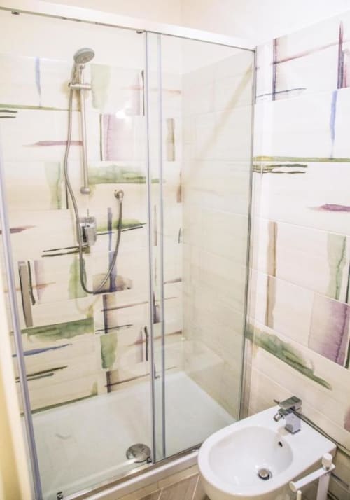 Ducha moderna con mamparas de cristal y pared de azulejos coloridos en el Borgo Angioino B&B de Nápoles