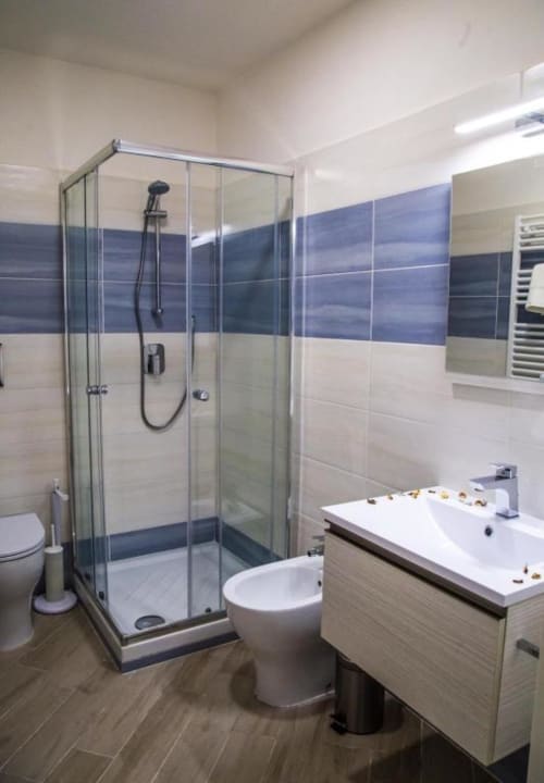 Baño moderno en Borgo Angioino en Nápoles con ducha acristalada, inodoro, lavamanos y azulejos azules.