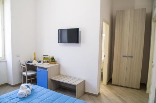 Luminoso dormitorio azul con escritorio, televisor de pantalla plana, armario y banco en Borgo Angioino en Nápoles