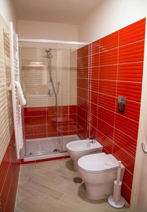 Baño moderno con paredes de azulejos rojos, inodoro y bidé blancos, ducha con mampara de cristal y suelo beige en Borgo Angioino B&B