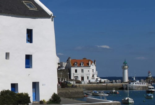 Bâtiment côtier blanc aux portes bleues surplombant le port, le phare et les bateaux à Belle Île-en-Mer, France