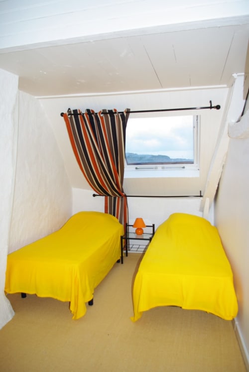 Chambre twin avec linge de lit jaune, rideaux rayés et vue sur mer à Belle Île en Mer